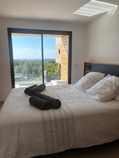 Chambre 6, suite parentale : la baie coulissante ouvre sur la terrasse, la mer à l’horizon.