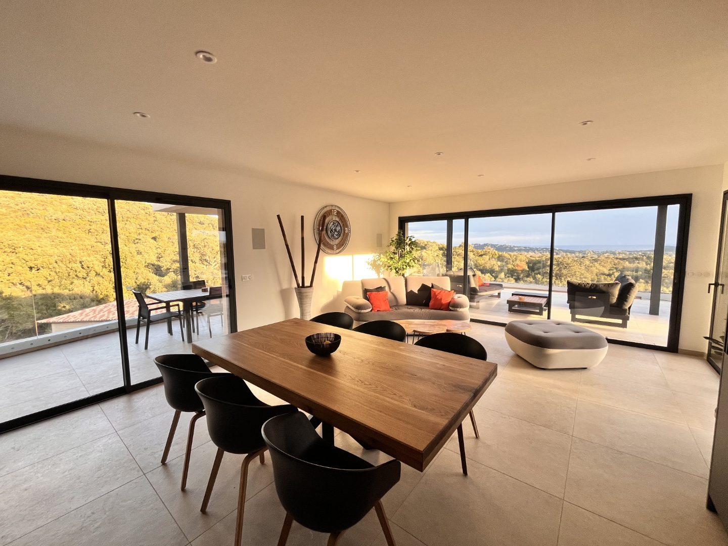 Le séjour du niveau supérieur : grande table en bois massif, salon ouvert et baies vitrées sur la terrasse.