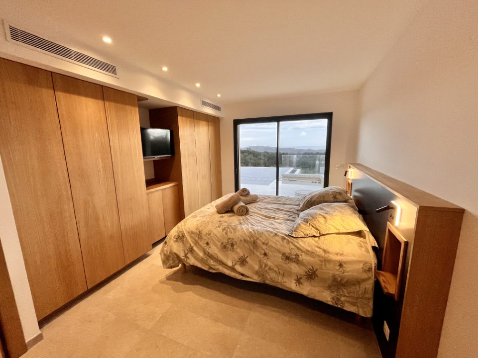 Chambre 3, suite parentale : lit double, mur de rangements en chêne et baie ouverte sur la terrasse.