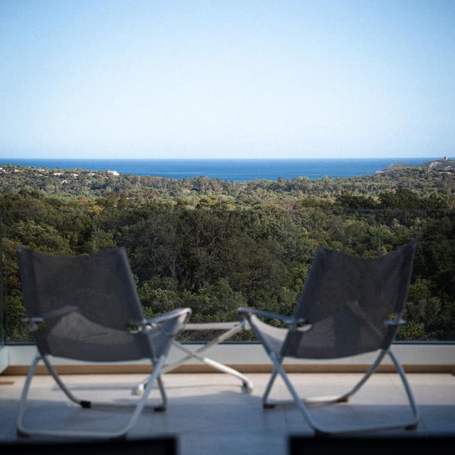 Deux fauteuils sur la terrasse de la villa, face au maquis et à la mer au loin.